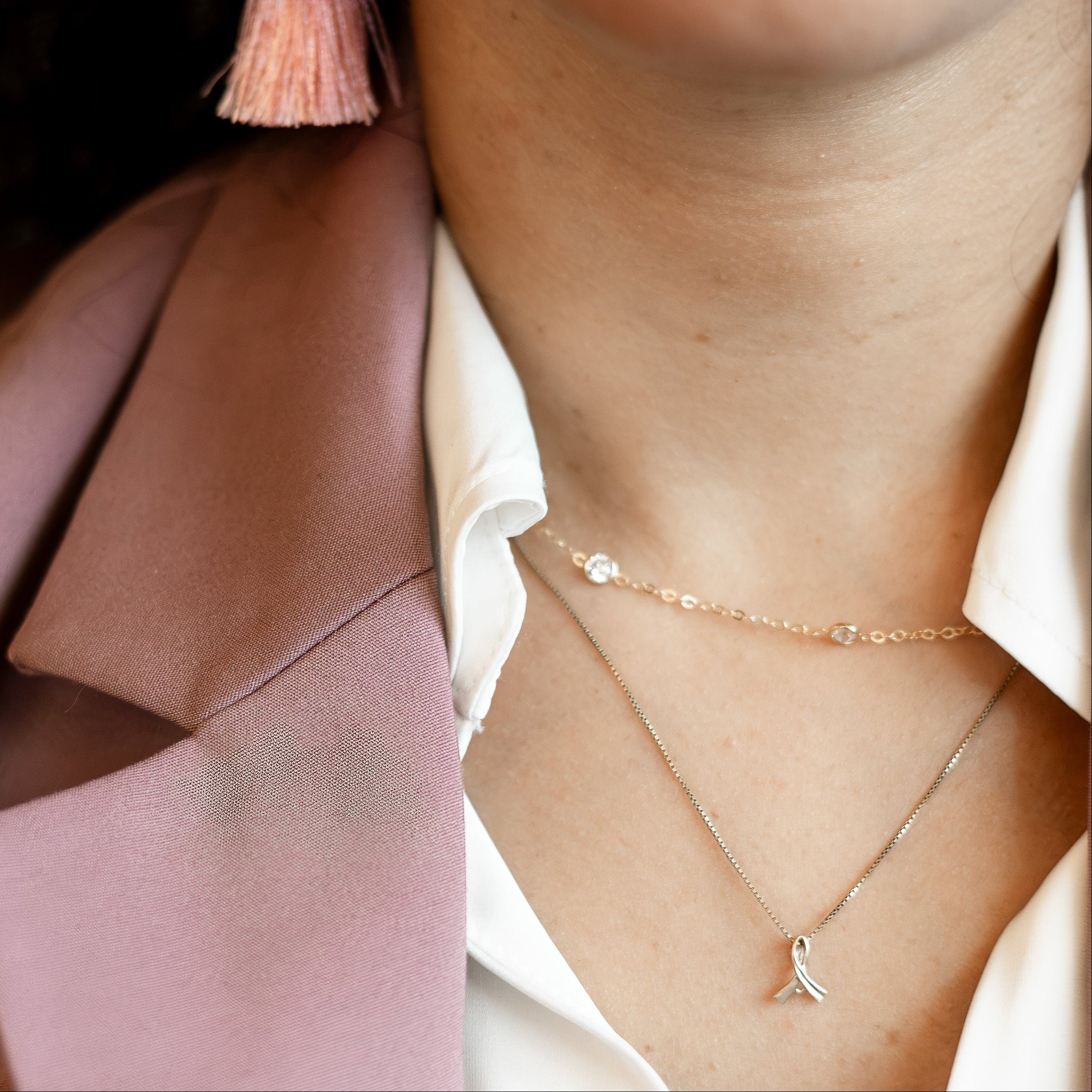 A close-up lifestyle shot of a woman wearing a tiered tassel earring in a dusty pink color, along with a white collared shirt and a mauve blazer.