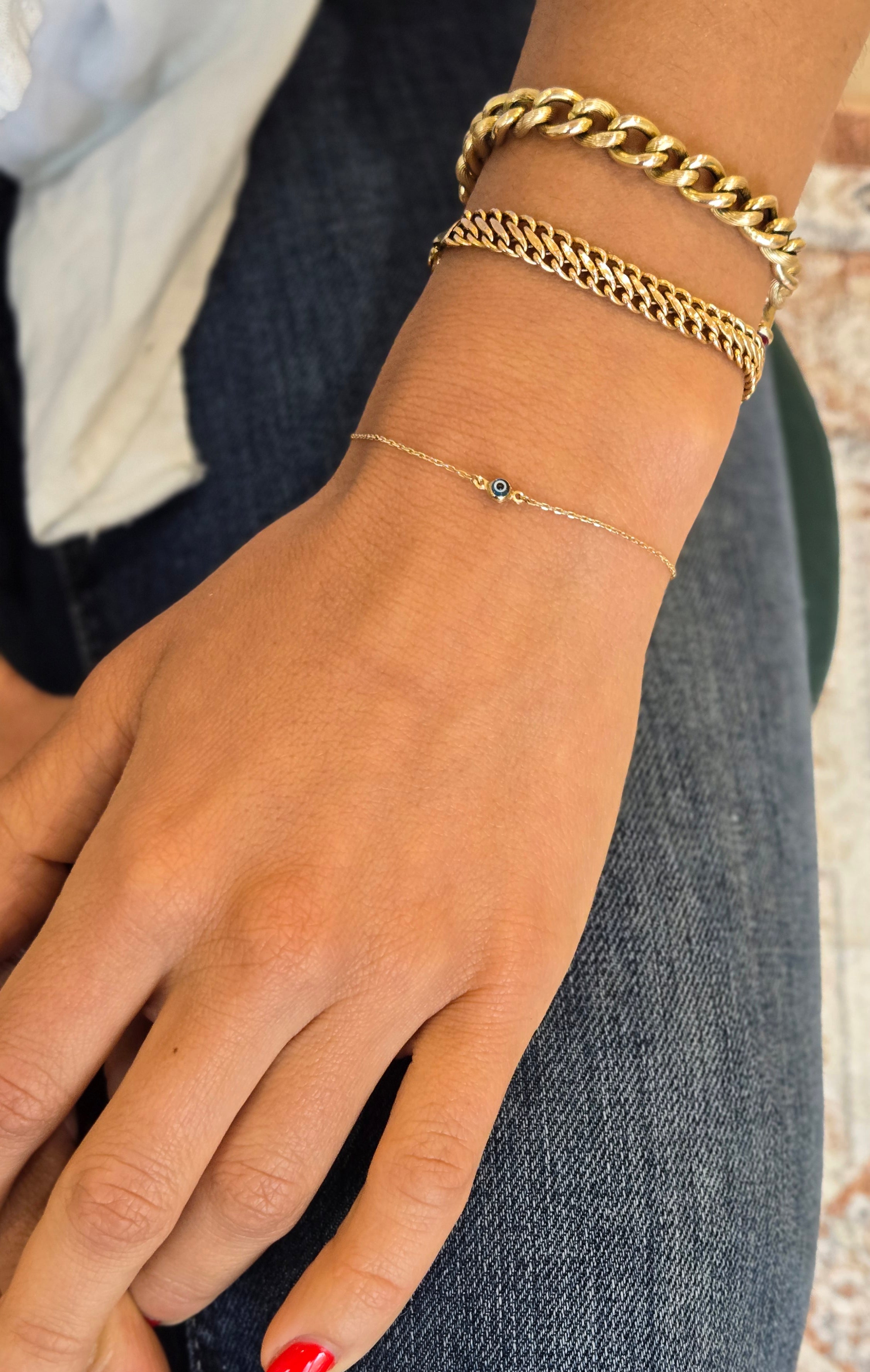 Hand wearing gold bracelets with red nail polish on a blurred background