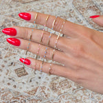Hand with red nail polish wearing multiple gold rings on a patterned background