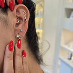 Close-up of a person's ear with earrings and hands with red nail polish.