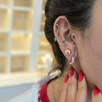 Close-up of a person's ear with multiple earrings, wearing a red top.