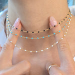 Close-up of a hand wearing multiple beaded necklaces with a blurred background
