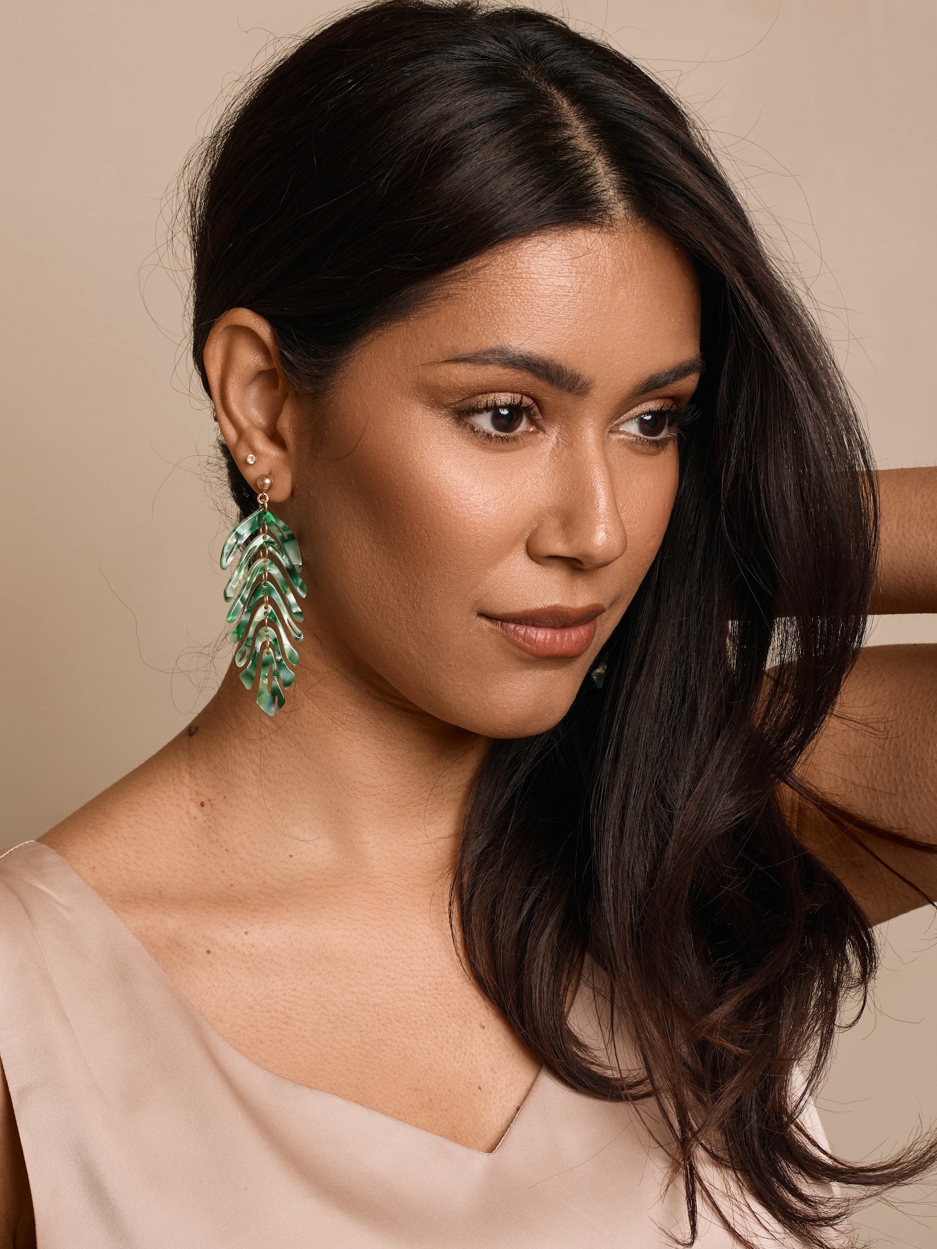 Woman wearing green leaf-shaped earrings against a neutral background