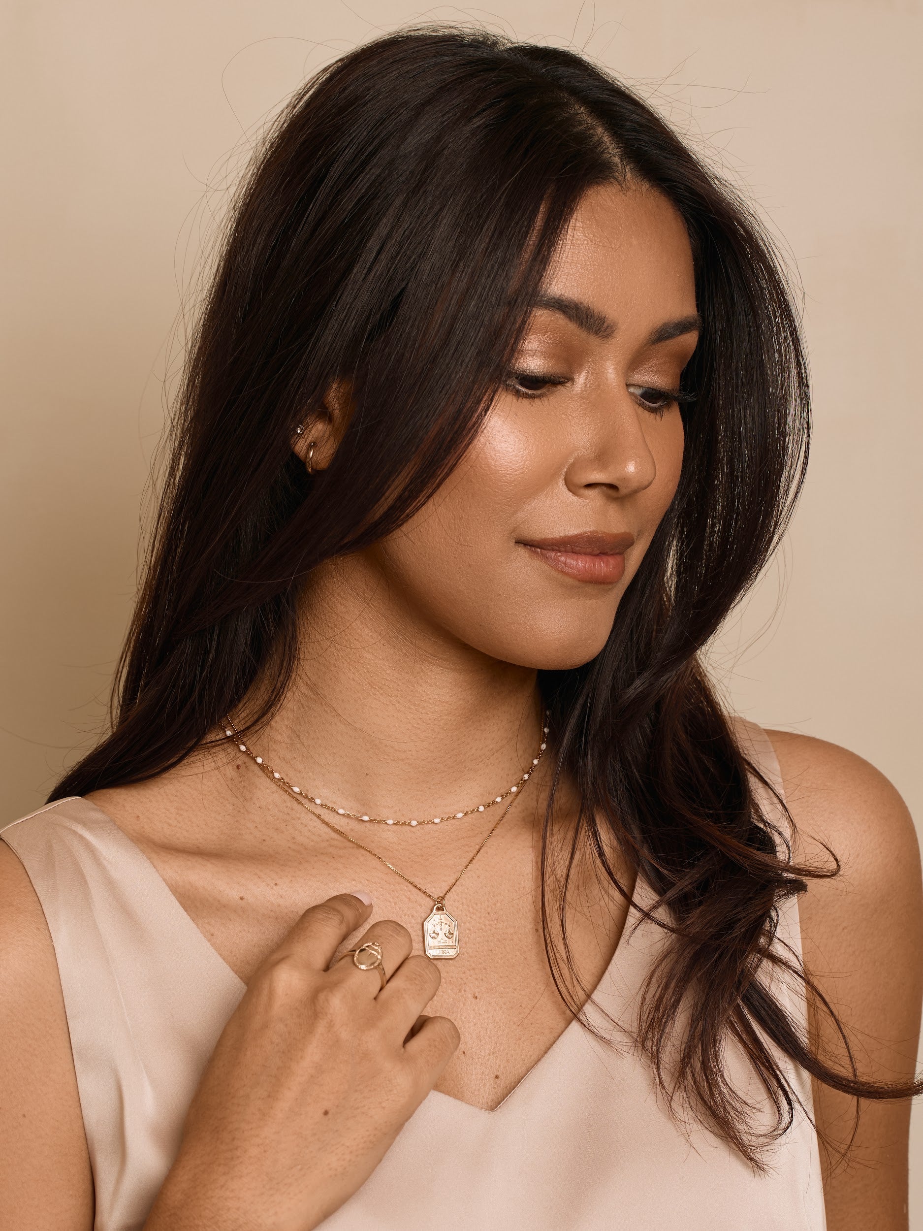 Woman wearing a necklace with a heart pendant against a beige background