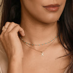 Woman wearing a gold necklace with a letter 'H' pendant against a neutral background