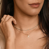 Woman wearing a gold necklace with a letter 'H' pendant against a neutral background