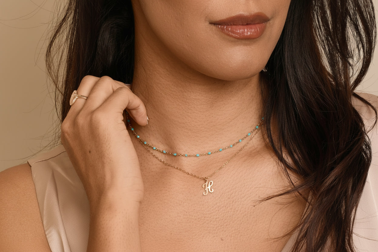 Woman wearing a gold necklace with a letter 'H' pendant against a neutral background