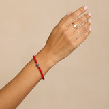 Hand wearing a red bracelet with a beige background
