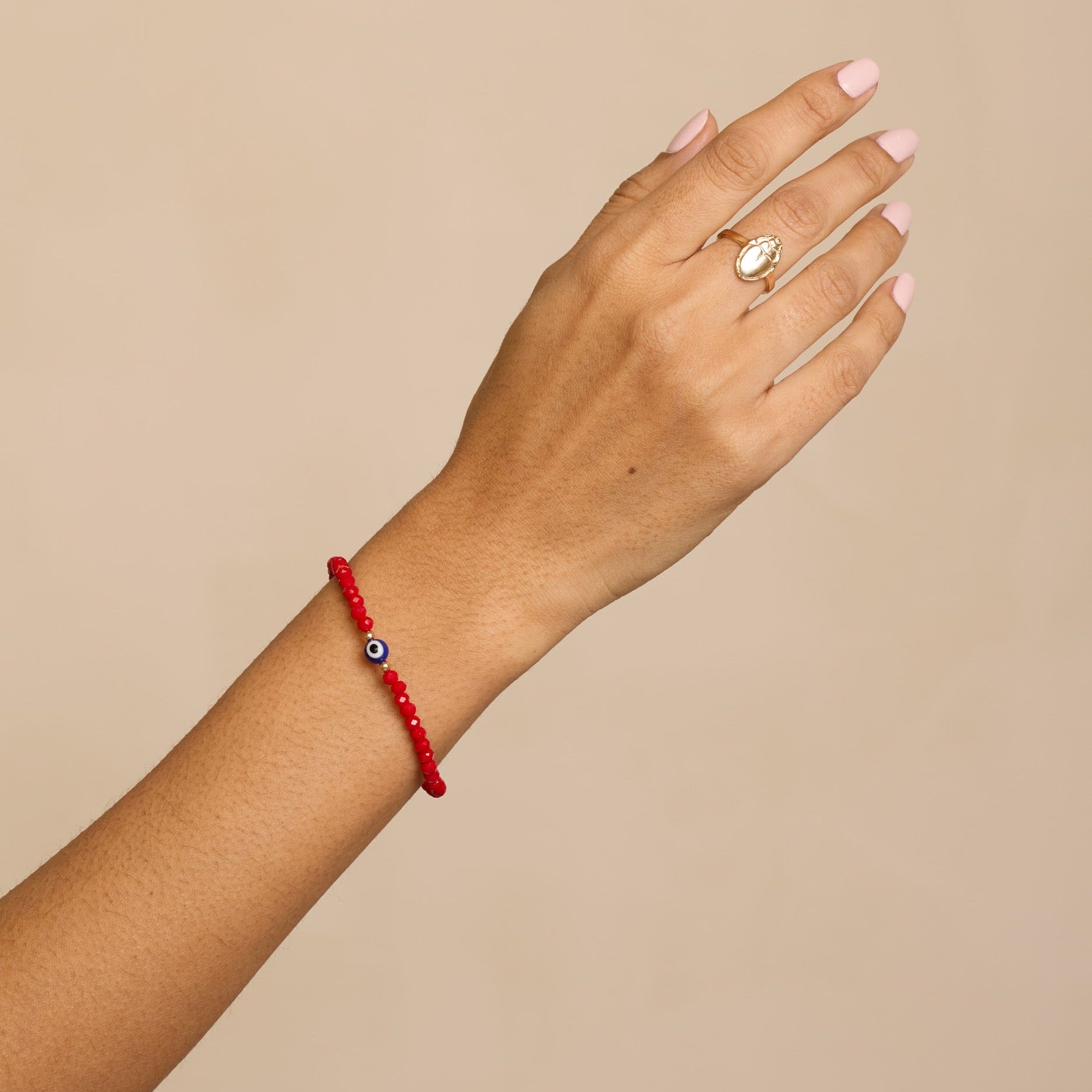 Hand wearing a red bracelet with a beige background