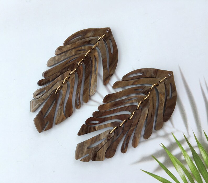 Pair of wooden leaf-shaped earrings on a white background with a green plant leaf.