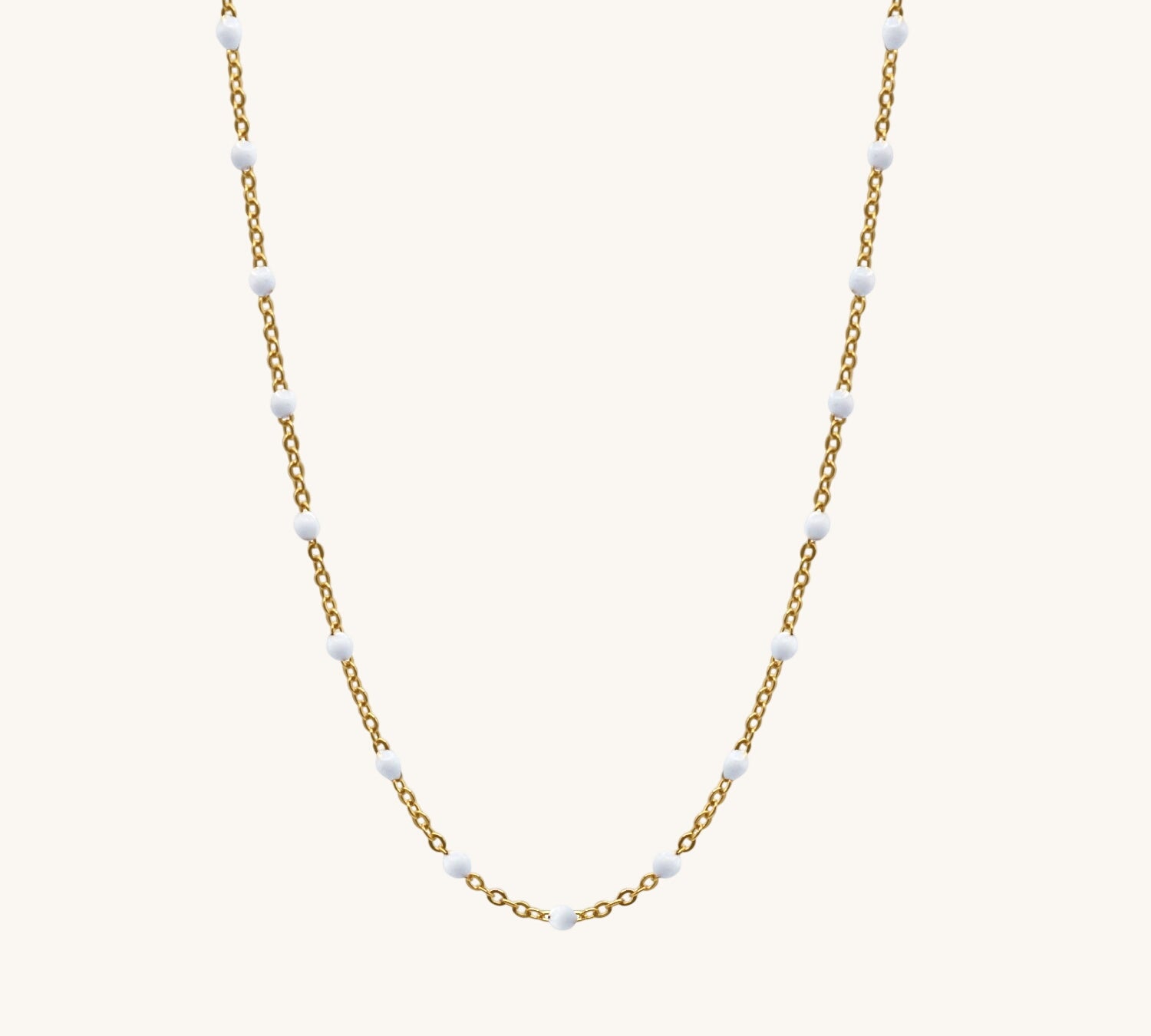 Gold chain necklace with small white beads on a white background