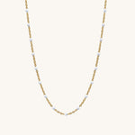 Gold chain necklace with small white beads on a white background