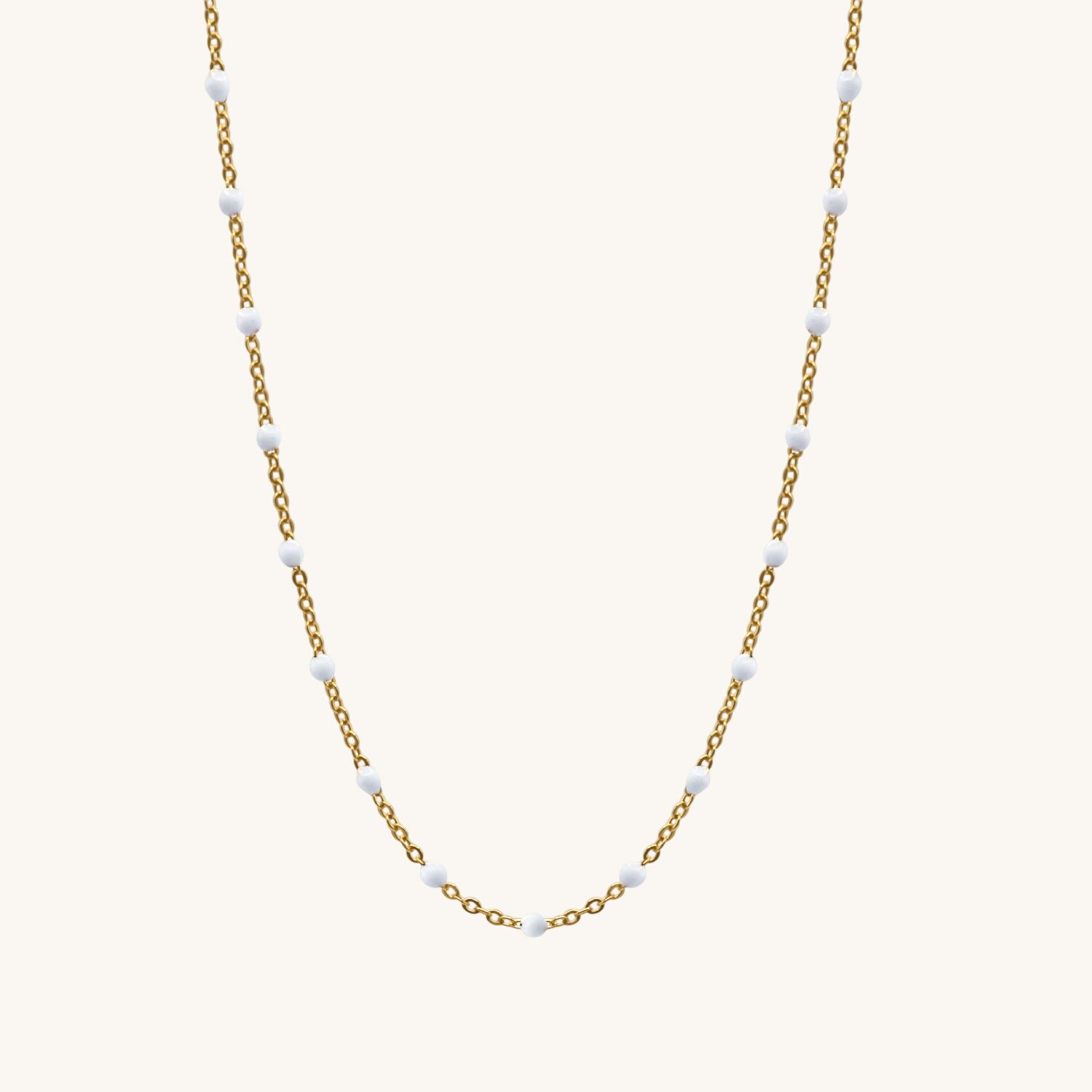 Gold chain necklace with small white beads on a white background