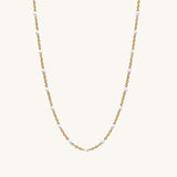 Gold chain necklace with small white beads on a white background