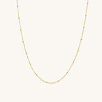 A gold satellite chain necklace laid out on a plain background.