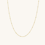 A gold satellite chain necklace laid out on a plain background.