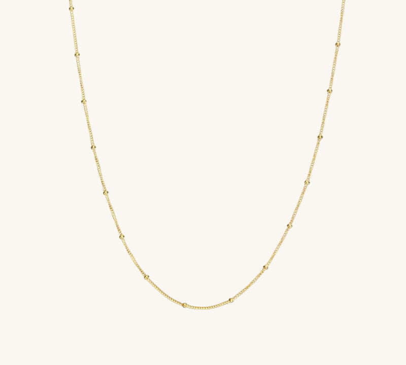 A gold satellite chain necklace laid out on a plain background.