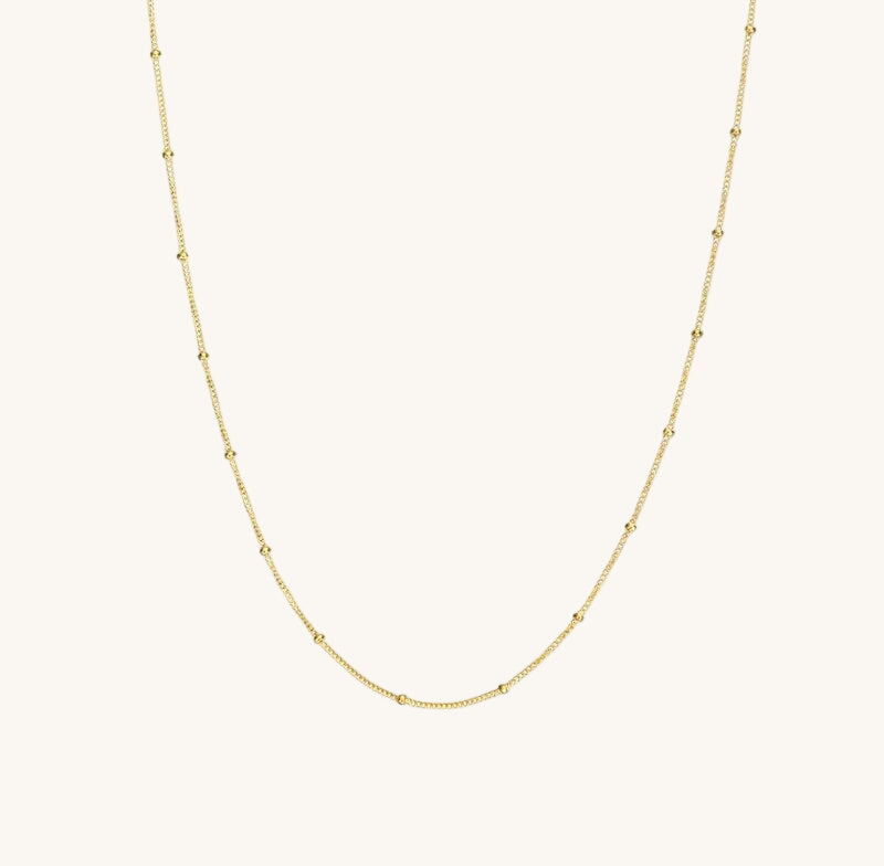 A gold satellite chain necklace laid out on a plain background.
