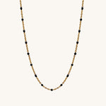 Gold chain necklace with black beads on a white background