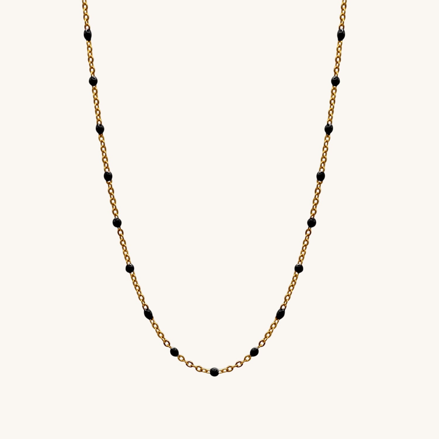 Gold chain necklace with black beads on a white background