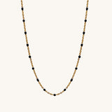 Gold chain necklace with black beads on a white background