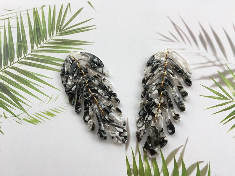 Pair of feather-shaped earrings on a white background with green palm leaves.